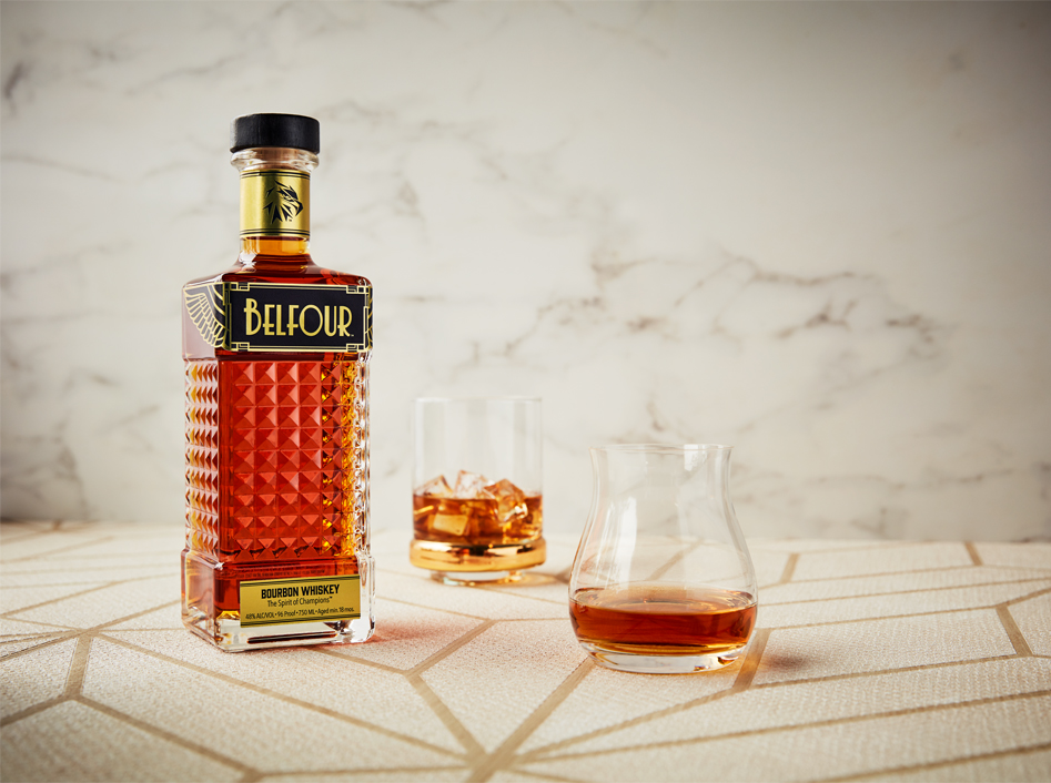 Belfour Bourbon bottle with metallic gold label with two glass on a light Art Deco table with a marble background
